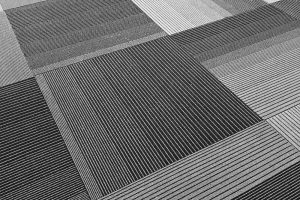 Black and white photo of a close-up of a section of carpet tiles. The carpet tiles have a striped pattern.