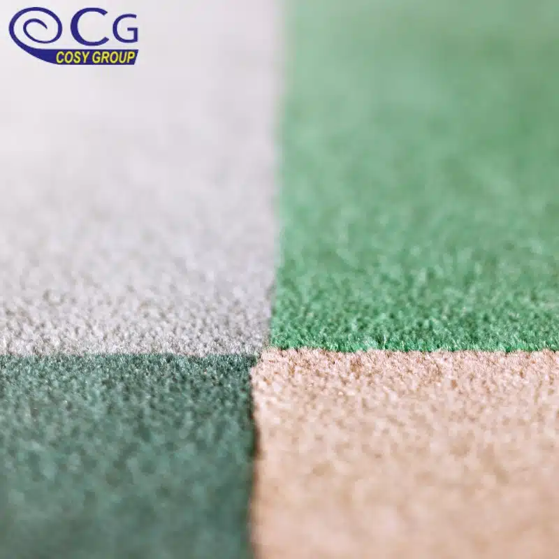 A close-up of carpet tiles in a checkerboard pattern with green, beige, and gray sections.