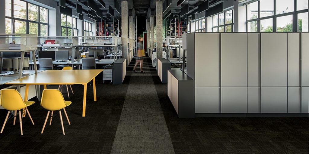 A modern office with yellow chairs, a yellow table, and dark carpet tiles.
