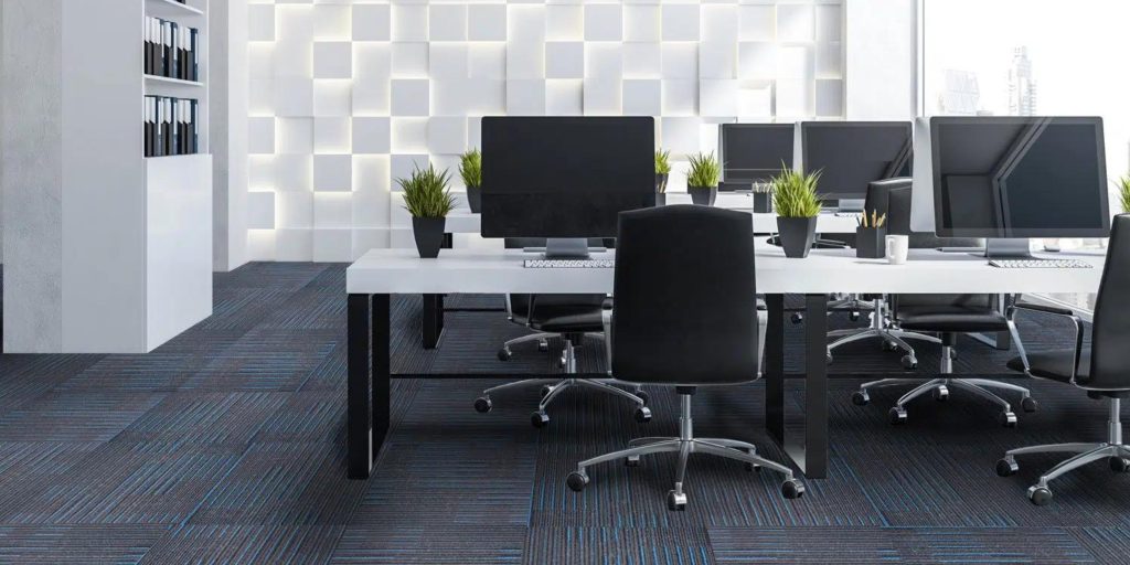 A modern office with blue and black carpet tiles, white desks, and a decorative illuminated wall.