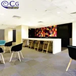 A modern office kitchen area with colorful carpet tiles, stools, and a vibrant geometric wall design.