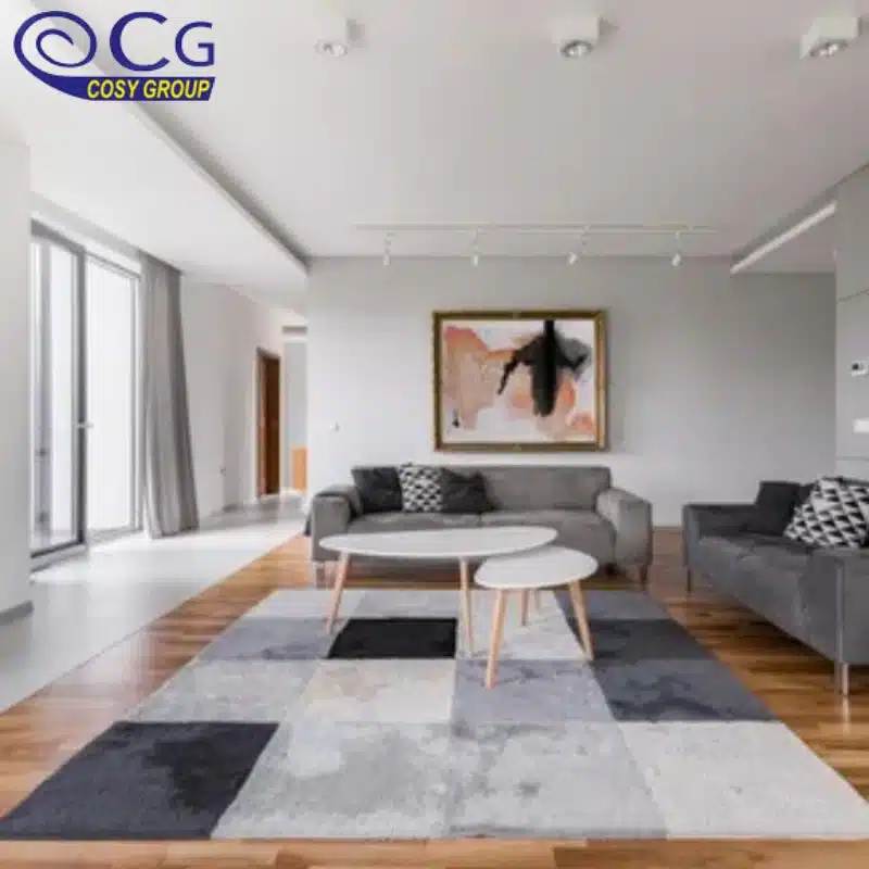 A modern living room with a gray sectional sofa, a coffee table, and a geometric rug in shades of gray and black.