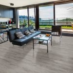 A modern living space with wood-look flooring, black leather sofa, and large windows with a scenic view.