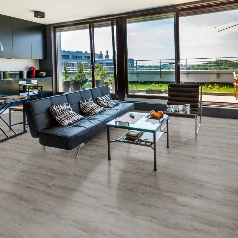 A modern living space with wood-look flooring, black leather sofa, and large windows with a scenic view.
