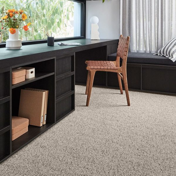 A modern workspace with a dark wooden desk, a woven chair, and a light carpet.