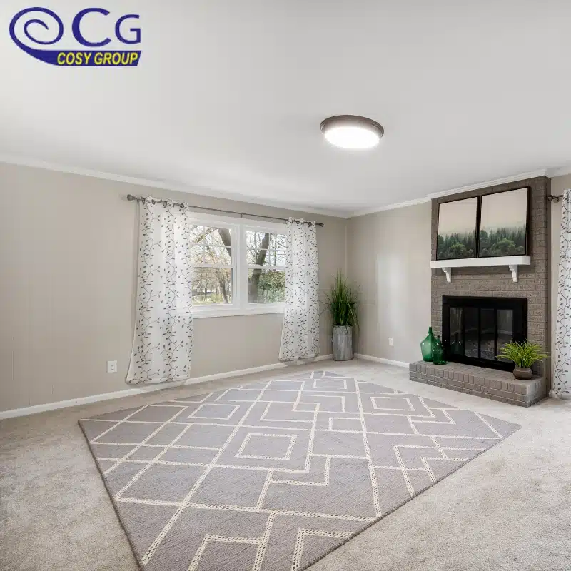A cozy living room with a gray geometric rug, large window, and a fireplace.