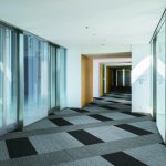 A modern office hallway with black and gray carpet tiles arranged in a checkered pattern.