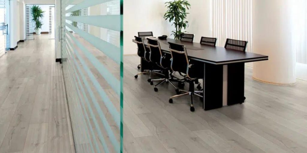 A modern office with light wood vinyl flooring, a glass partition, and a conference table with office chairs.