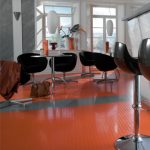 A modern café or dining space with vibrant orange and gray vinyl flooring, contemporary furniture, and large windows.
