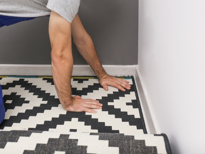 Installing carpet tile on concrete with hands pressing patterned tile near wall