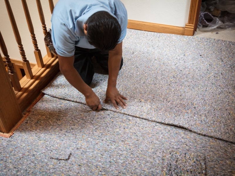 Professional installer preparing floor with underlay for carpet tile installation.